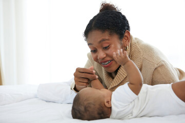 Wall Mural - African young mother playing with her adorable baby on bed