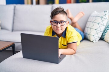 Sticker - Adorable hispanic boy using laptop lying on sofa at home