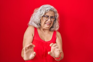 Canvas Print - Middle age woman with grey hair standing over red background disgusted expression, displeased and fearful doing disgust face because aversion reaction.