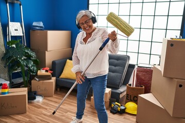 Poster - Middle age woman listening to music and playing paint roller as a guitar at new home