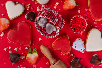 High-colored bright red Valentine day baking background, Various bakery ingredients, cookies, chocolates, sugar sprinkles, strawberry, rolling pin and whisk, for cooking valentine`s sweets, desserts