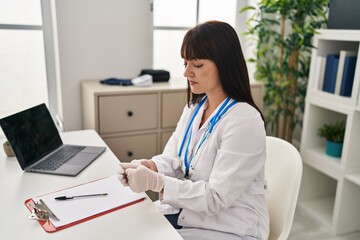 Young beautiful hispanic woman doctor wearing gloves at clinic