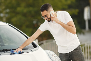 Indian man wiping his white transportation on car wash after washing