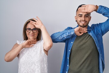 Poster - Hispanic mother and son standing together smiling cheerful playing peek a boo with hands showing face. surprised and exited