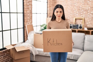 Sticker - Young woman moving to a new home holding box relaxed with serious expression on face. simple and natural looking at the camera.