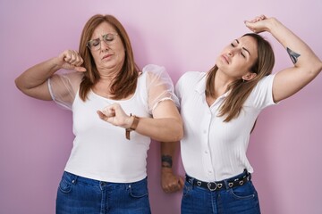 Poster - Hispanic mother and daughter wearing casual white t shirt over pink background stretching back, tired and relaxed, sleepy and yawning for early morning