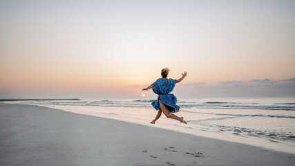 Wall Mural - Young woman enjoying time at sea, jumping.