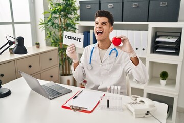 Wall Mural - Young hispanic doctor man supporting organs donations angry and mad screaming frustrated and furious, shouting with anger looking up.