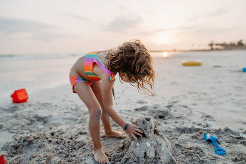 Wall Mural - Little girl playing on the beach, building sand castle.