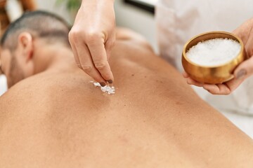 Canvas Print - Young hispanic man having back massage using salt at beauty center