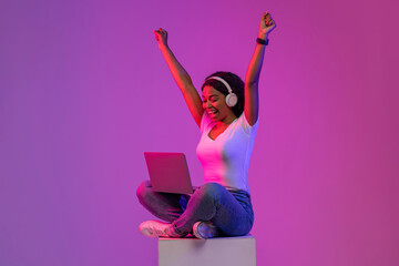 Online Win. Happy Black Woman Celebrating Success With Laptop In Neon Light
