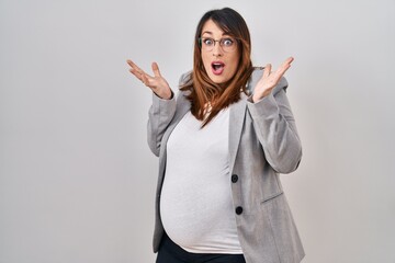 Poster - Pregnant business woman standing over white background celebrating victory with happy smile and winner expression with raised hands