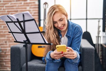 Sticker - Young blonde woman musician using smartphone sitting on sofa at music studio