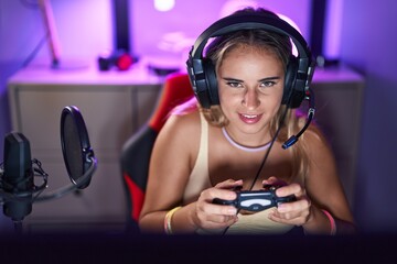 Wall Mural - Young blonde woman streamer playing video game using joystick at gaming room