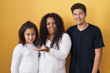 Sticker - Family of mother, daughter and son standing over yellow background pointing aside with hands open palms showing copy space, presenting advertisement smiling excited happy