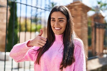 Wall Mural - Young hispanic woman smiling confident doing ok sign with thumb up at street