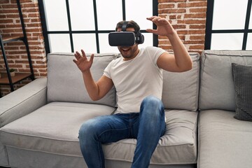 Wall Mural - Young hispanic man playing video game using virtual reality glasses at home