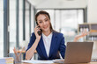 © amnaj - Beautiful smiling Asian businesswoman talking on mobile phone while working in office.