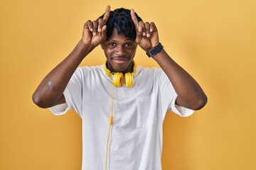 Sticker - Young african man with dreadlocks standing over yellow background doing funny gesture with finger over head as bull horns