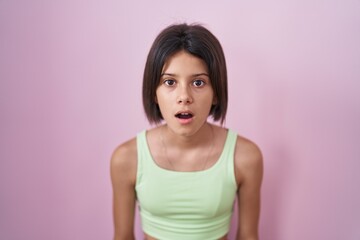 Poster - Young girl standing over pink background afraid and shocked with surprise and amazed expression, fear and excited face.