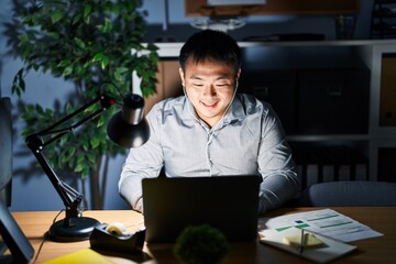 Canvas Print - Young chinese man working using computer laptop at night with a happy and cool smile on face. lucky person.