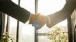 © Yuliia - Close-up two men shake hands in office near window sunny sun background. Unrecognizable partners diverse businessmen conclude successful agreement support partnership cooperation greeting handshaking