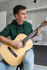 Wall Mural - One young man Caucasian teenager sit at home in room playing guitar