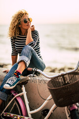 Wall Mural - Pretty woman sitting outdoor with a bike having relax leisure activity with beach in background. One female people healthy rider lifestyle. Transport and sustainability environment. Happiness freedom