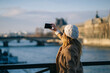© Daniel Gonzalez/Stocksy - Young woman taking selfie on bridge during holidays
