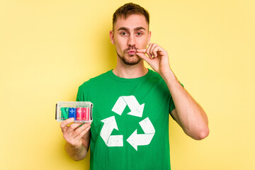 Wall Mural - Young man holding batteries to recycle them cut out isolated with fingers on lips keeping a secret.