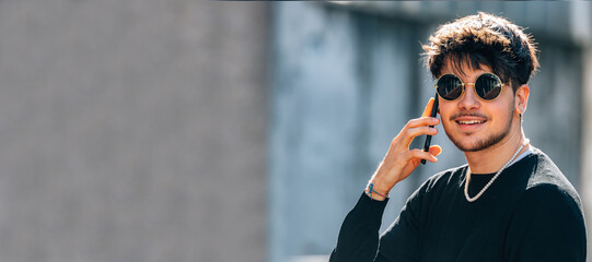 Wall Mural - portrait of young man with sunglasses in the street talking on mobile or cell phone