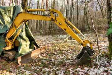 Excavator left in woodland and covered in tarpaulin for snow protection
