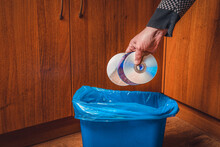 A Man Throws CDs Into The Trash Can. Man's Hand With CDs And Trash Can In Blue