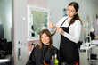 Focused young woman professional hair stylist working with female client, making haircut with scissors in hairdressing studio..