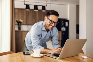 a smiling developer typing on the code on the laptop while working from home.