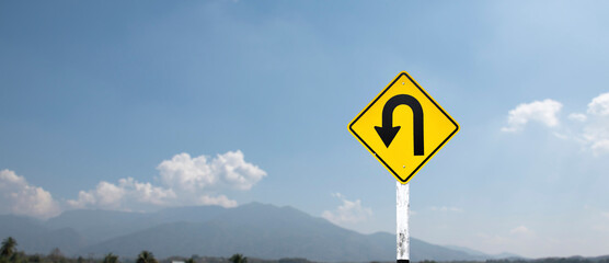 Traffic sign: left U-turn sign on cement pole beside the rural road with white cloudy bluesky background, copy space.	