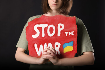 Poster - Sad woman holding poster with words Stop the War on black background, closeup