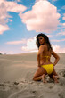Back view beautiful woman in yellow bikini kneeling on sand 