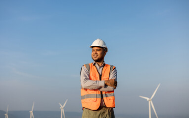 Engineer India man working at windmill farm Generating electricity clean energy. Wind turbine farm generator by alternative green energy. Asian engineer checking control electric power