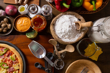 Bag with flour and wooden scoop on a wooden table in a rustic kitchen. Top view the ingredients for homemade pizza on wooden table.