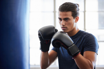 Wall Mural - Man, boxing and fitness in gym exercise for power, performance and cardio against a window background. Boxer, fighter and athletic male training on punching bag at sports center, serious and tough