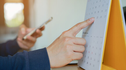 close up on businessman hand using pen to writing schedule on calendar 2023 to make appointment meeting or manage timetable each day at house for work from home concept