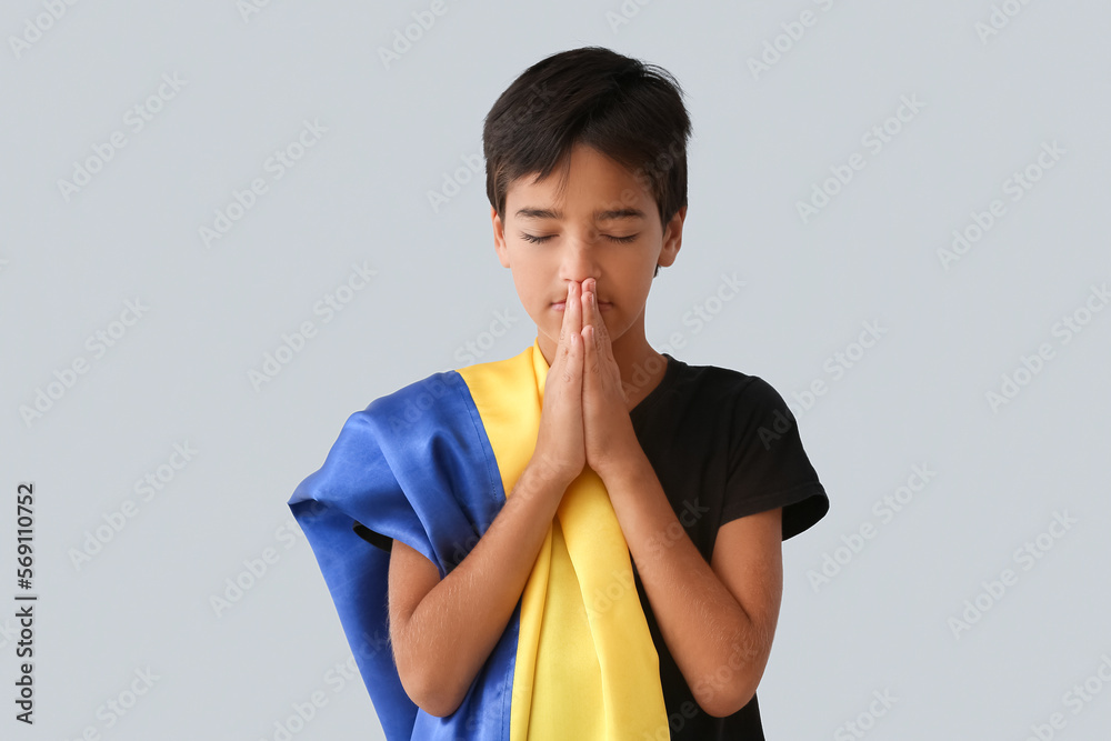 Little boy with flag of Ukraine praying on light background