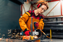 Woman In STEM Using Grinder To Cut A Metal Bar, Wearing Gloves And A Apron With Protective Sleeves. She's Making A New Metal Part For Her Engineering Project