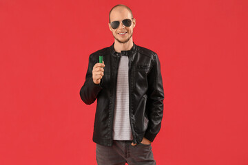 Wall Mural - Young man in sunglasses with disposable electronic cigarette on red background