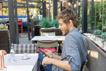 Wall Mural - Young man with beard using smarthphone in a cafe bar