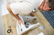 Unrecognizable senior plumber installer installing toilet drain flange in a house.