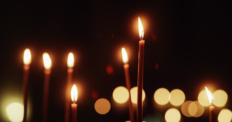 Wall Mural - Cinematic Shot of Candles with Flames Burning on Black Background with Bokeh Lights. Warm Aesthetic Atmosphere Representing Hope and Peace. Candles Lit as Part of Religious Ritual or Memorial Service