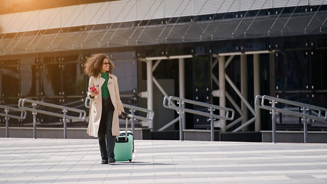 young african woman walking outdoors carrying a suitcase and going to travel by airplane at modern a