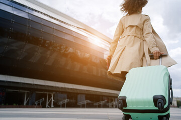 Young african woman walking outdoors carrying a suitcase and going to travel by airplane at modern airport. Vacations, travel and active lifestyle concept    